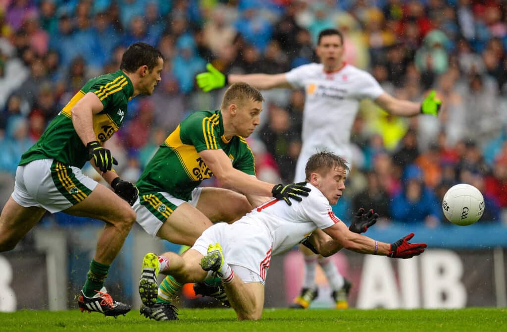 A Tyrone Gaelic football player making a pass while under pressure from two Kerry players. Similarities between Gaelic football and American football might have something to do with the growth of the NFL in Ireland.