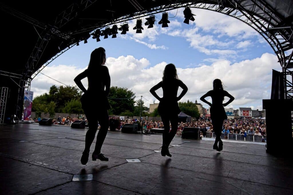 Three Irish dancers shot from behind perform on stage at a festival.