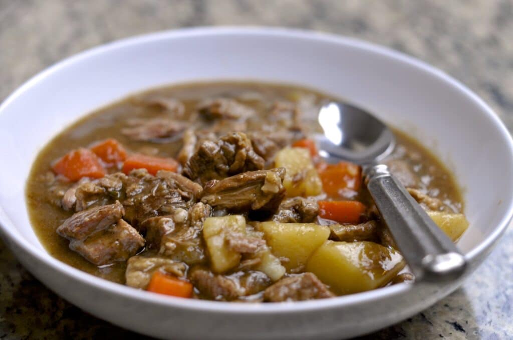 A bowl of Irish stew with lamb, potatoes, and carrots, and a fork resting in the stew.