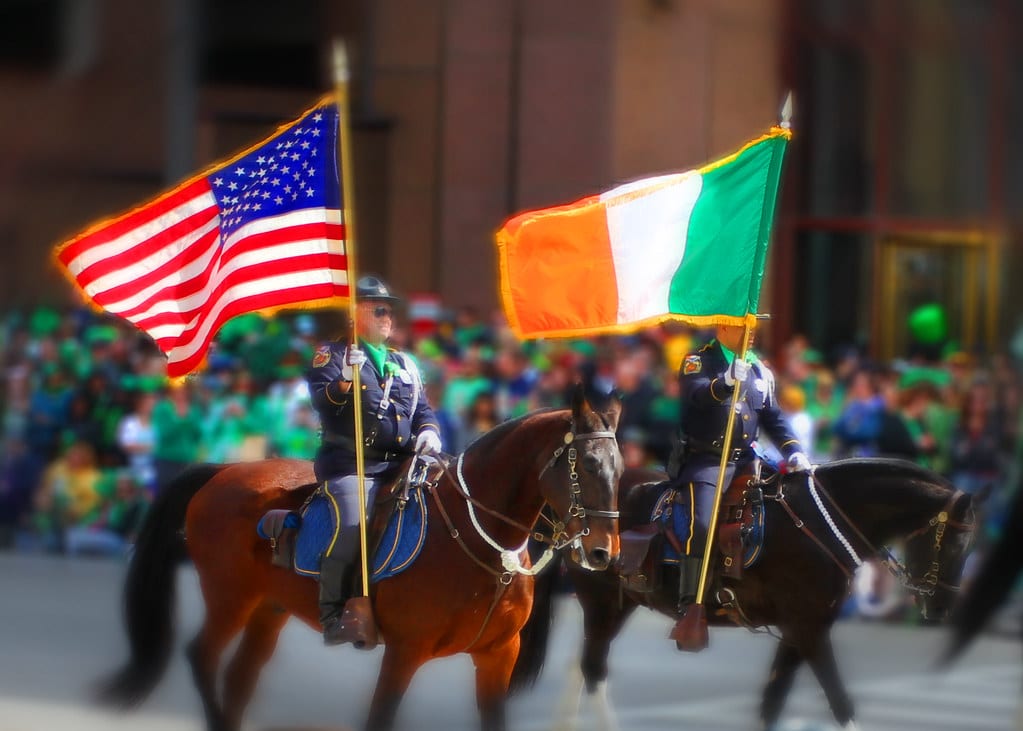 Picture of the American and Irish flags held by men on a horse. Used to explain why Americans are obsessed with Ireland: Understanding the connection.