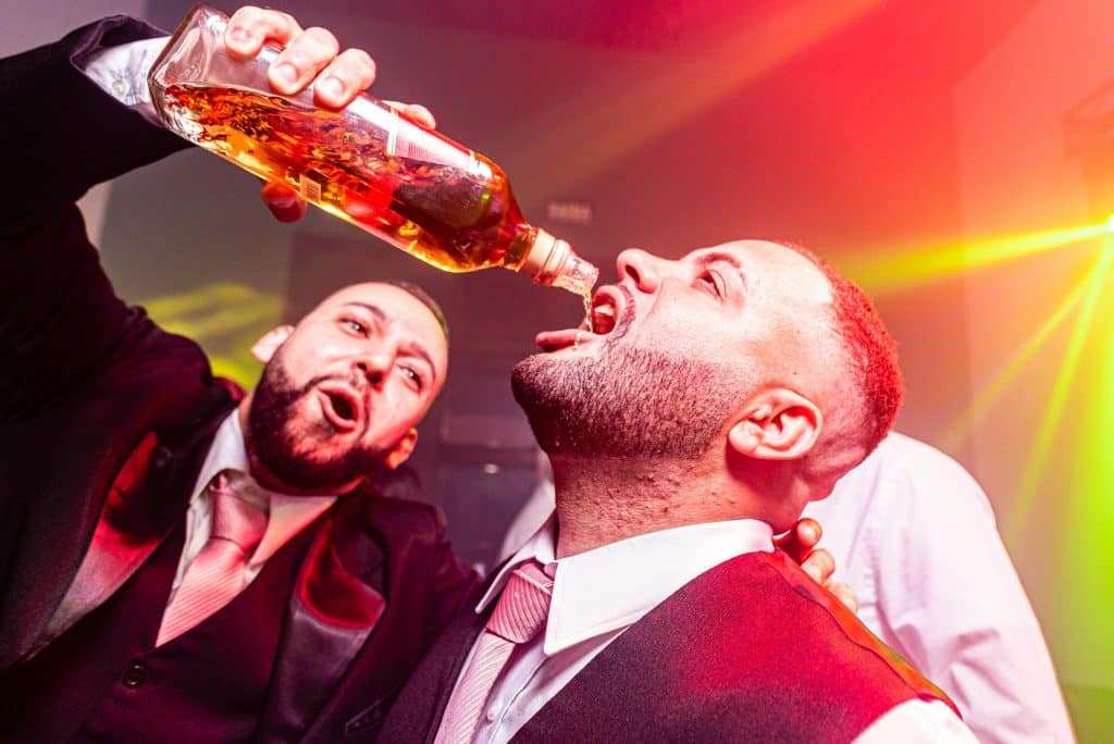 Picture of a man pouring a bottle of drink into another mans mouth.