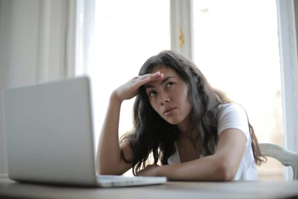 A woman holding her head and rolling her eyes in front of a computer screen.