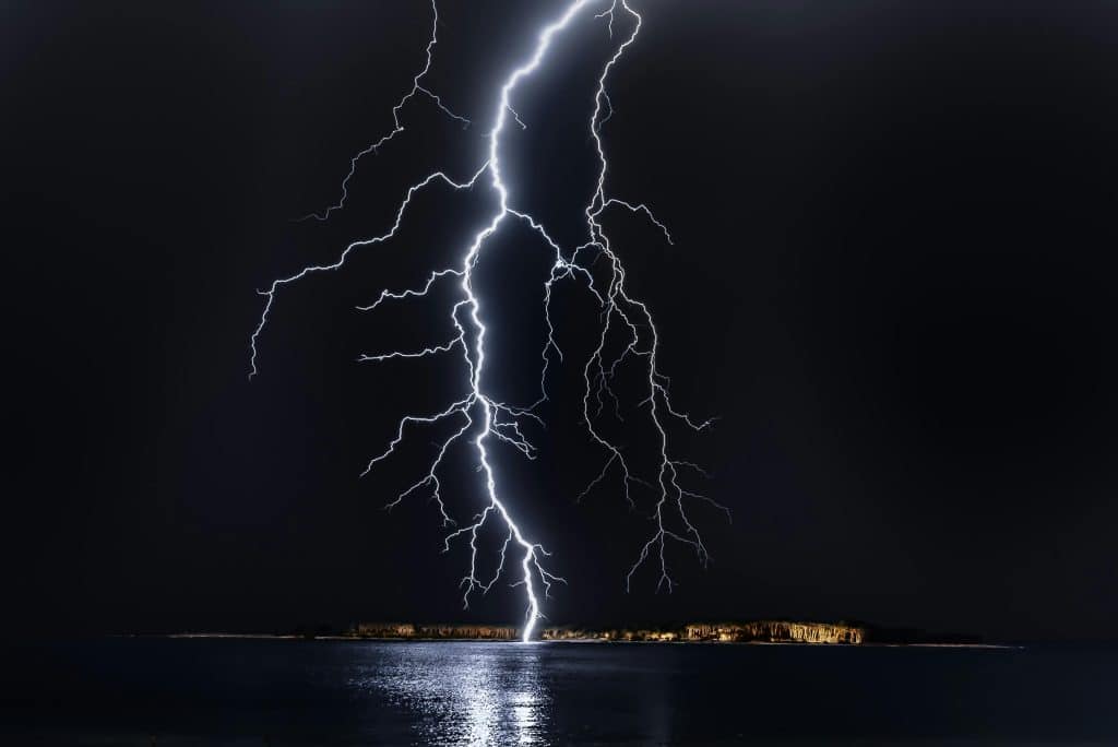 Lightning striking the sea at night just in front of a small island.