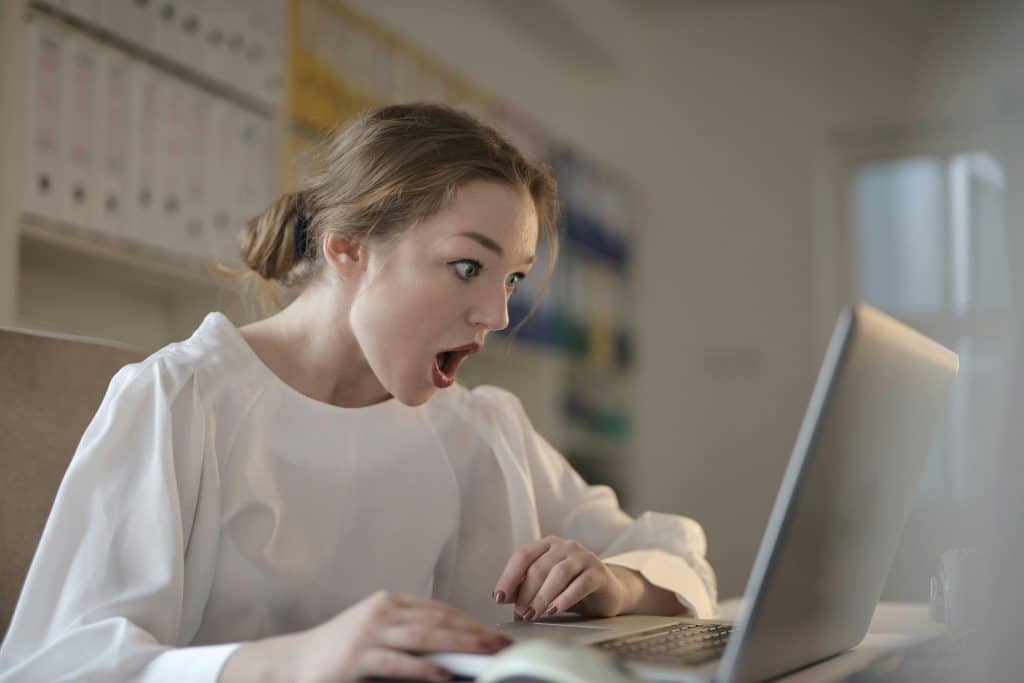 A woman looking at a computer screen with a shocked face.