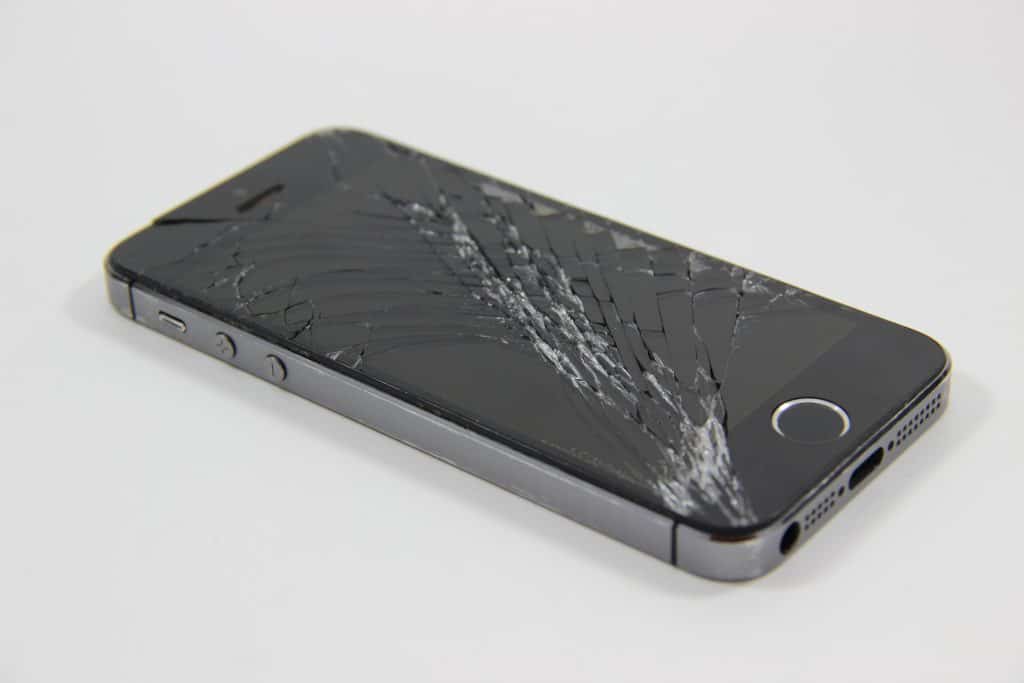 A black smartphone with a severely shattered screen rests on a plain white surface.