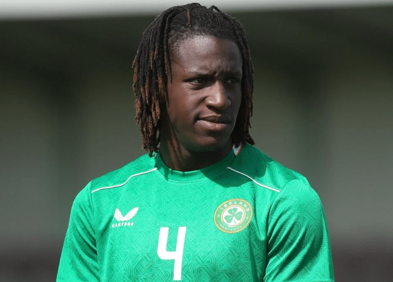A close-up portrait of Bosun Lawal looking off-camera while wearing a green Republic of Ireland training top.
