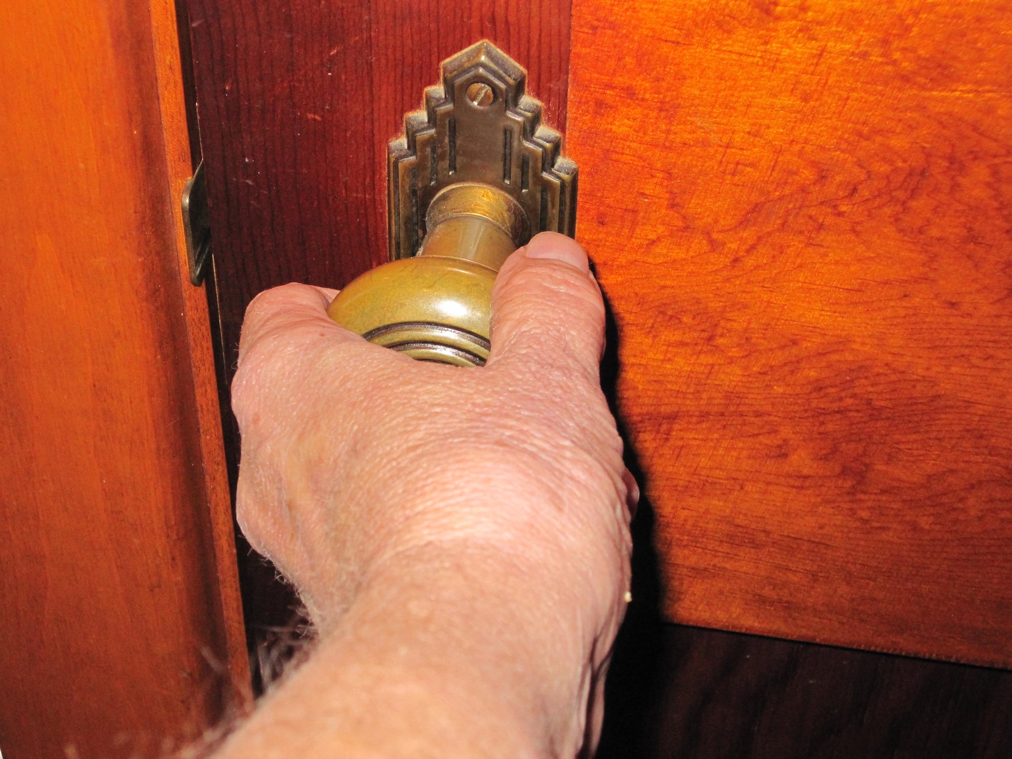 A close-up shot of a hand grasping a brass doorknob on a polished wooden door, captured mid-turn.