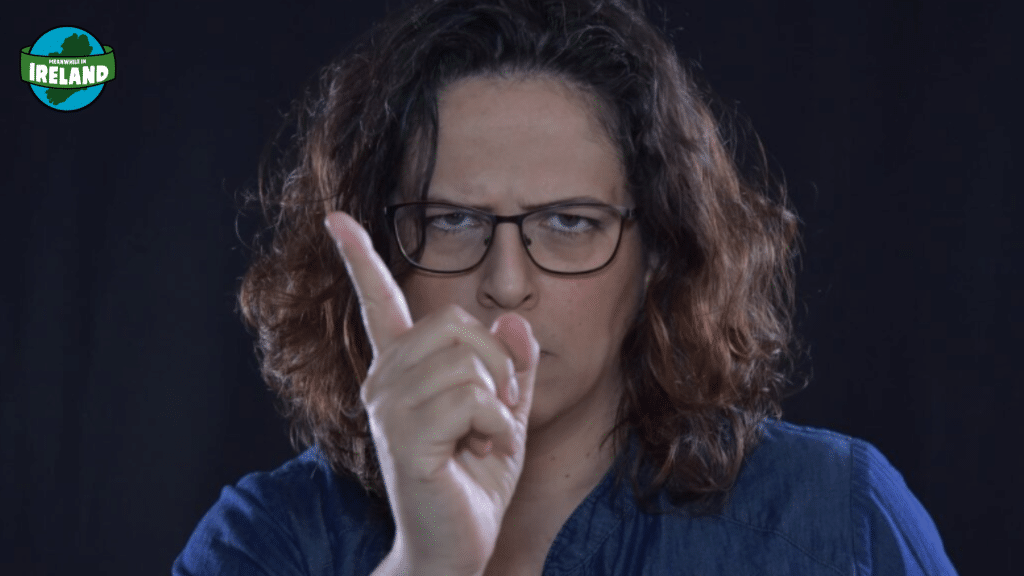 A woman with glasses and curly hair pointing a finger forward with a stern, warning expression.