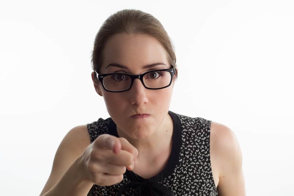 Angry woman with glasses pointing at the camera.