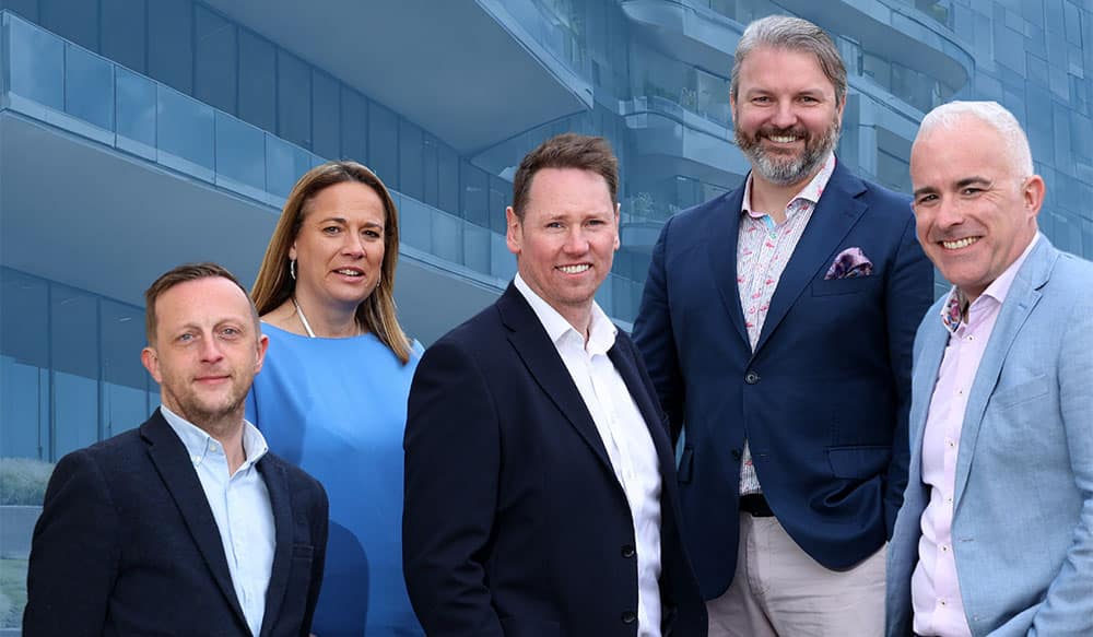 The leadership team of ID-Pal standing in front of an office building, identified from left to right as: James O'Toole (CBO), Shelley McKinney (CMO), Colum Lyons (CEO), Simon Montgomery (COO), and Robert O'Farrell (CTO).