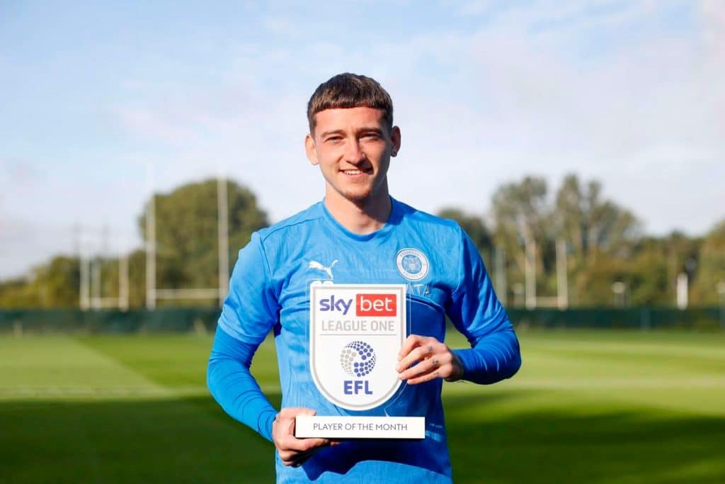 Louie Barry smiling while holding up a "Sky Bet League One Player of the Month" award on a football training pitch.