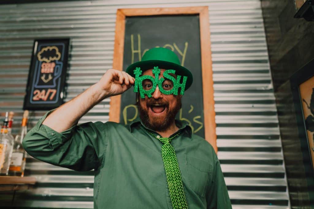 Man wearing a green hat, green shits, and fun glasses that say Irish.
