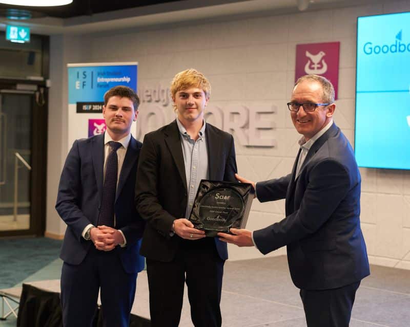 Ryan Ormonde (centre) receives the Enterprise Ireland Student Entrepreneur of the Year award from a presenter while his business partner stands to his left.