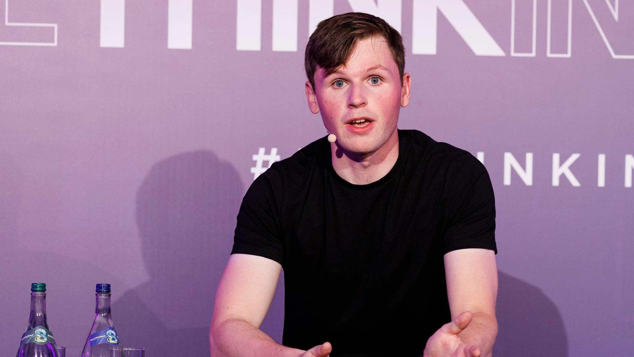 Shane Curran speaking at a conference, seated in front of a purple backdrop.