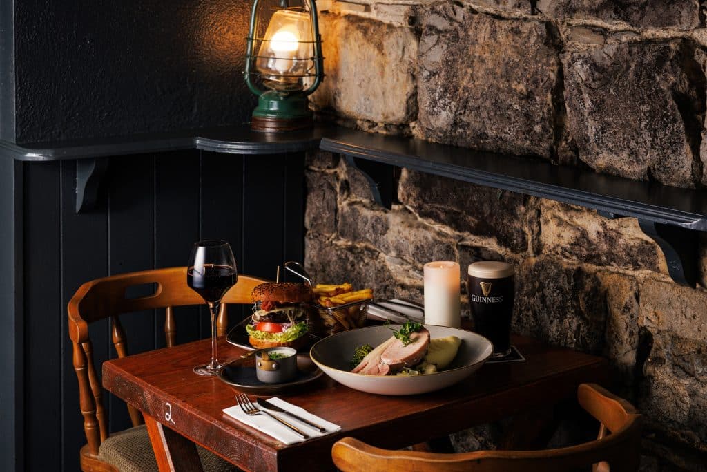 A meal with a pint of Guinness and a glass of red wine against a stone wall of a pub.