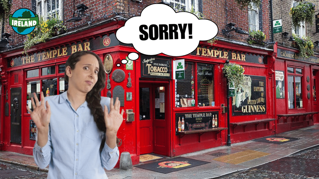 A woman with a confused expression holds up her hands in front of the iconic red Temple Bar in Dublin. A thought bubble above her head contains the word "SORRY!"